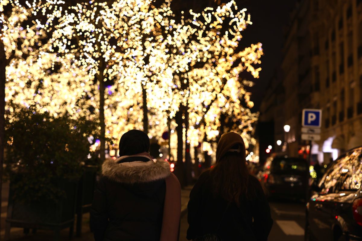 People strolling beneath Christmas-lit trees on a Paris avenue